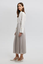 Model wearing a high-waisted pleated maxi skirt styled with a white blouse and pointed heels.