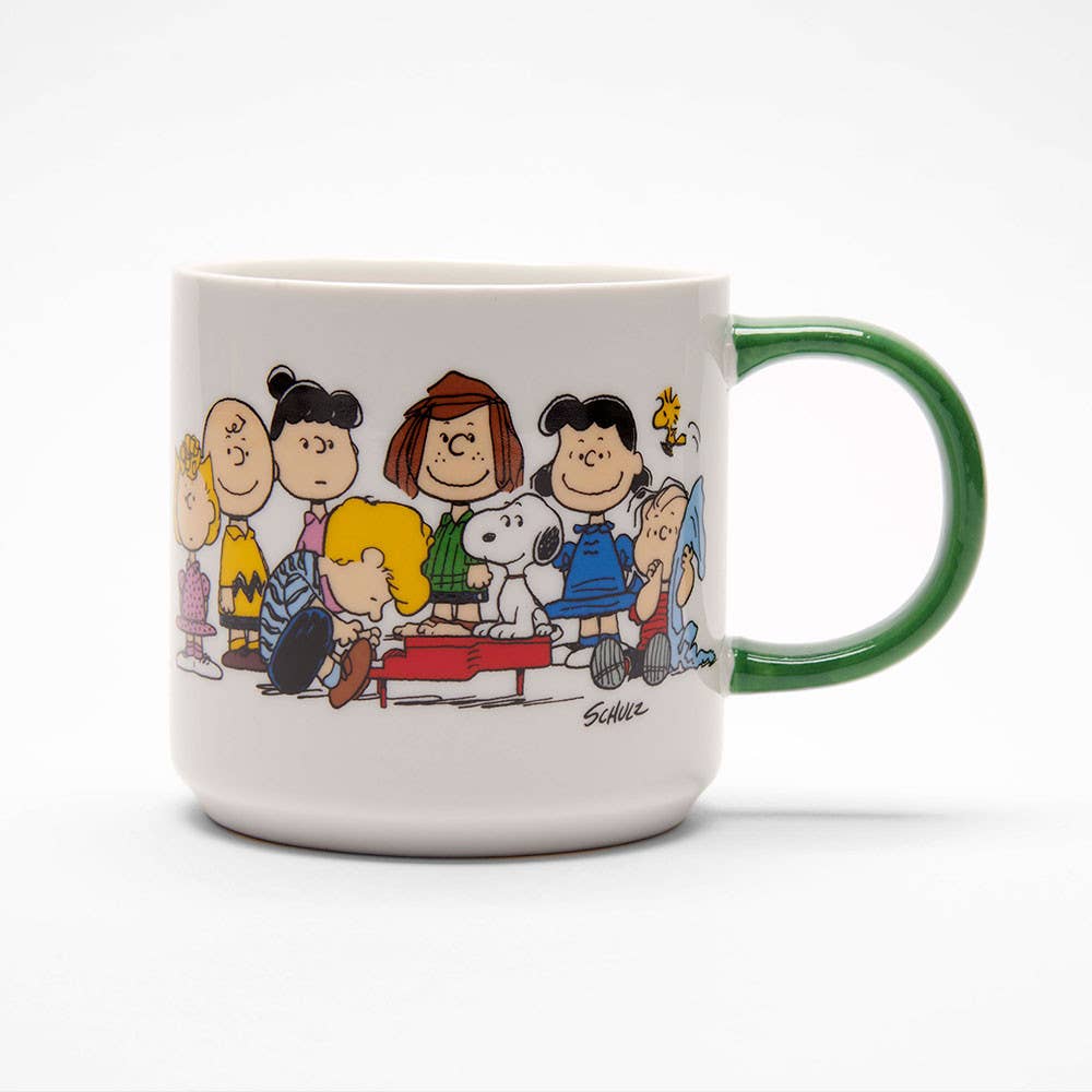 White ceramic mug with a green handle, featuring a beagle and a bird on a red doghouse, along with a group of characters enjoying music.