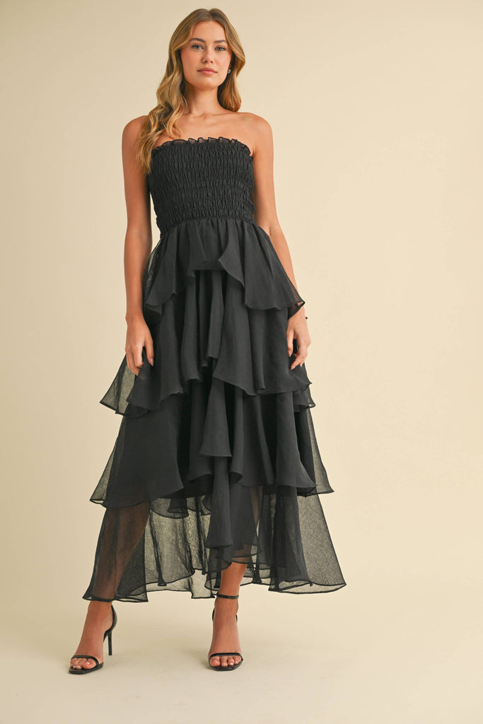 Woman wearing a strapless ruffled maxi dress with a smocked bodice, available in taupe and black.