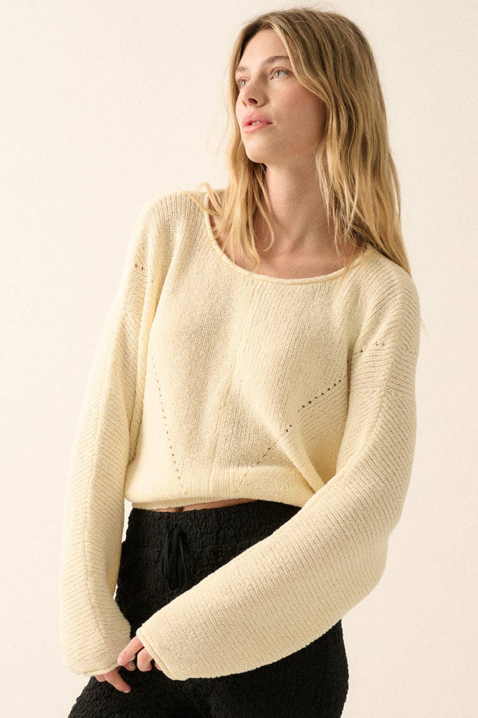 Woman wearing a cream lightweight knit sweater with wide sleeves and a cropped fit.