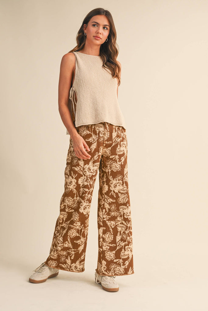 Woman wearing a beige ribbed knit tank top with side ties, paired with floral wide-leg pants