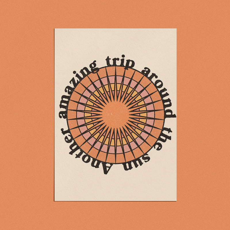 A greeting card with a retro-style sunburst design and the phrase "Another amazing trip around the sun" in bold, circular text.