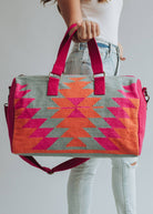 Vibrant weekender bag with orange and hot pink geometric design, held by woman in light wash jeans and white tank top