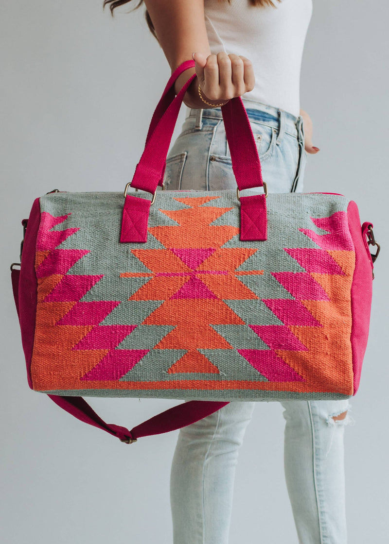 Vibrant weekender bag with orange and hot pink geometric design, held by woman in light wash jeans and white tank top