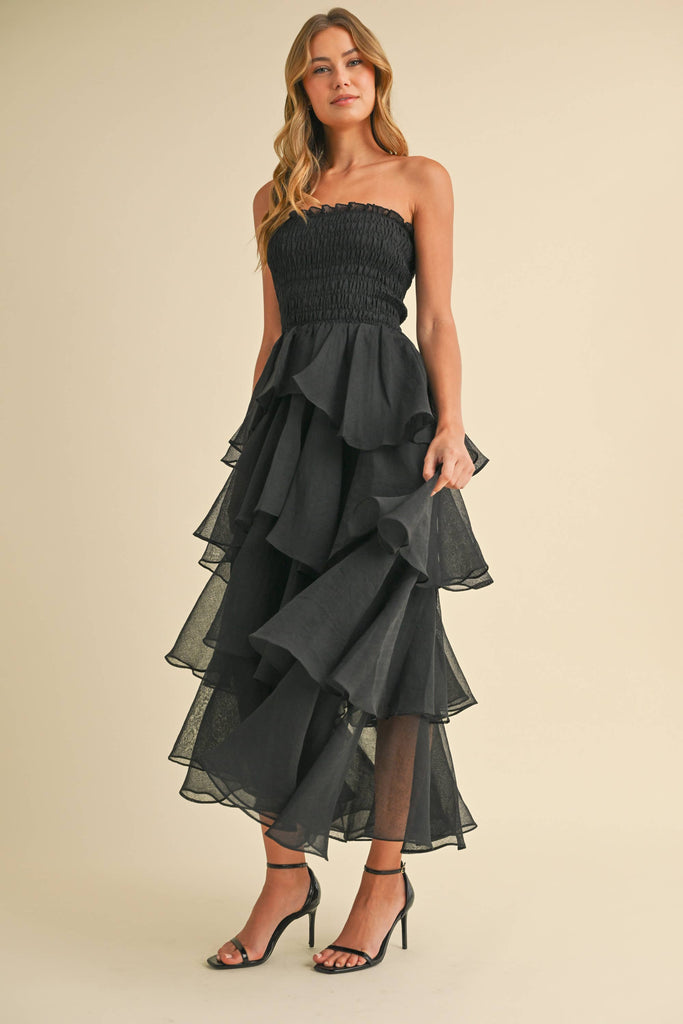Woman wearing a strapless ruffled maxi dress with a smocked bodice, available in taupe and black.