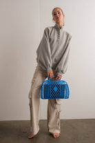 Woman wearing an oversized gray pullover sweatshirt with quarter snaps and voluminous sleeves, paired with beige pants.