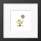 Framed print of a cheerful yellow bird holding a pink flower, set in a white mat with a black frame for a simple, elegant look.