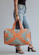 Wool woven orange and sage green weekender bag with geometric pattern, held by woman in jeans and black top