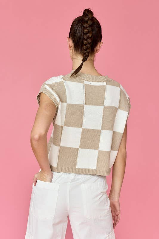 Woman wearing a taupe and white loose-fit checker knit top with white pants.