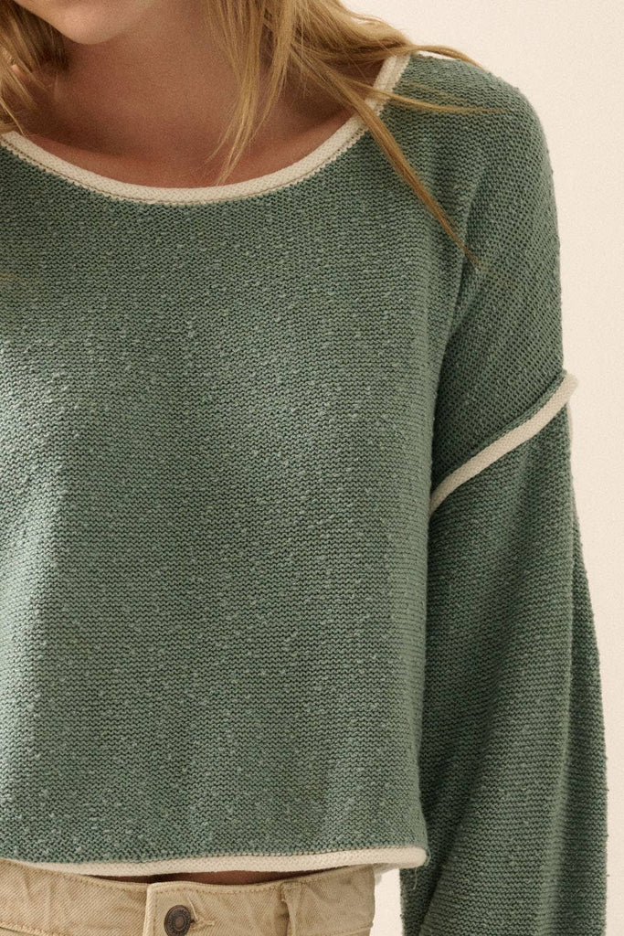 Woman wearing a sage green off-shoulder cropped sweater with white trim details and long sleeves.