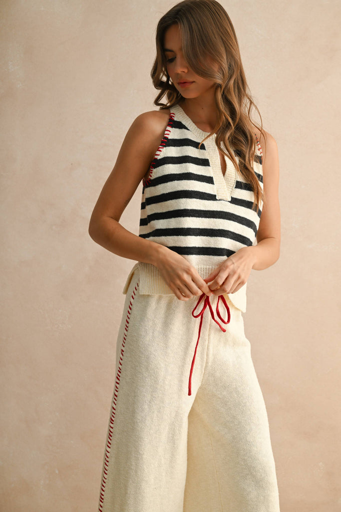 Woman wearing a cream knit set with striped sleeveless top and wide-leg pants with red drawstring.