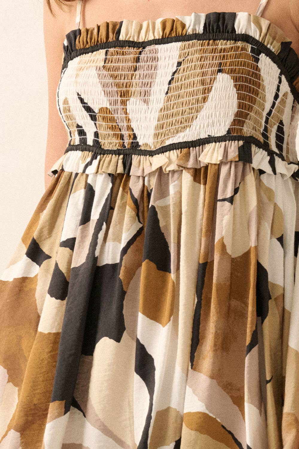 Woman wearing an abstract printed romper in warm earth tones with a smocked bodice and flowy shorts.