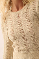 Woman wearing a beige knit romper with bell sleeves, scalloped hems, and open-weave detailing.