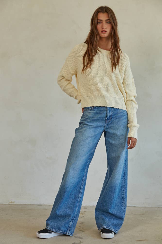 Woman wearing a cream chunky knit pullover sweater with relaxed fit, styled casually with light-wash jeans.
