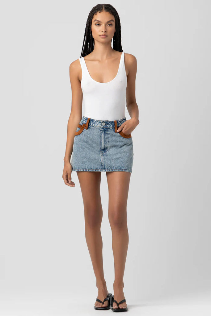 Woman wearing a white tank top and denim skirt on a plain background