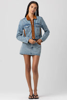 Woman wearing a denim jacket with brown collar on a white background