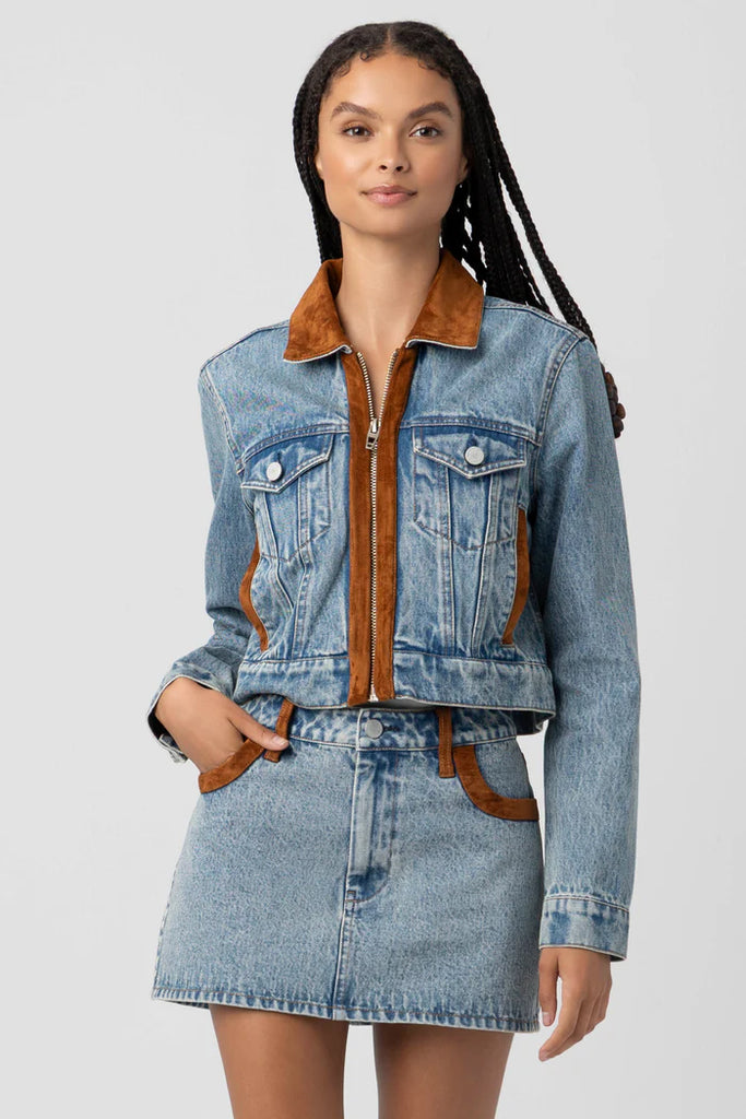 Woman wearing a denim jacket with brown interior and matching skirt on a light gray background