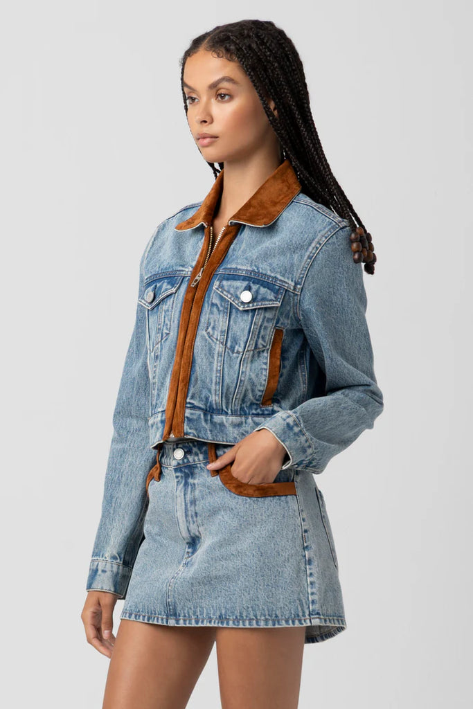 Woman wearing a denim jacket with brown collar on a gray background