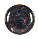 A round ceramic jewelry dish with a celestial design, including golden moons, stars, and constellations on a dark background.