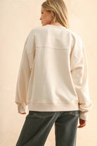 Woman wearing a cream sweater with bold red embroidered “Paris” lettering, paired with dark denim jeans.