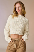 Woman wearing a cream popcorn knit cropped sweater with tan drawstring pants, hands in pockets.