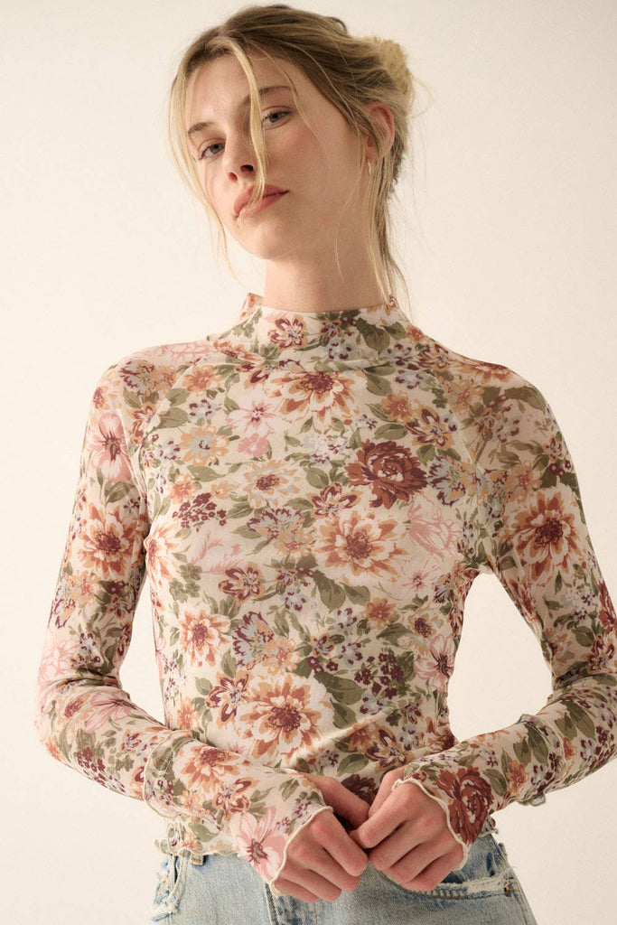 Woman wearing a sheer mesh floral long-sleeve top with mock neck and fitted silhouette.