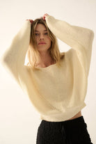Woman wearing a cream lightweight knit sweater with wide sleeves and a cropped fit.