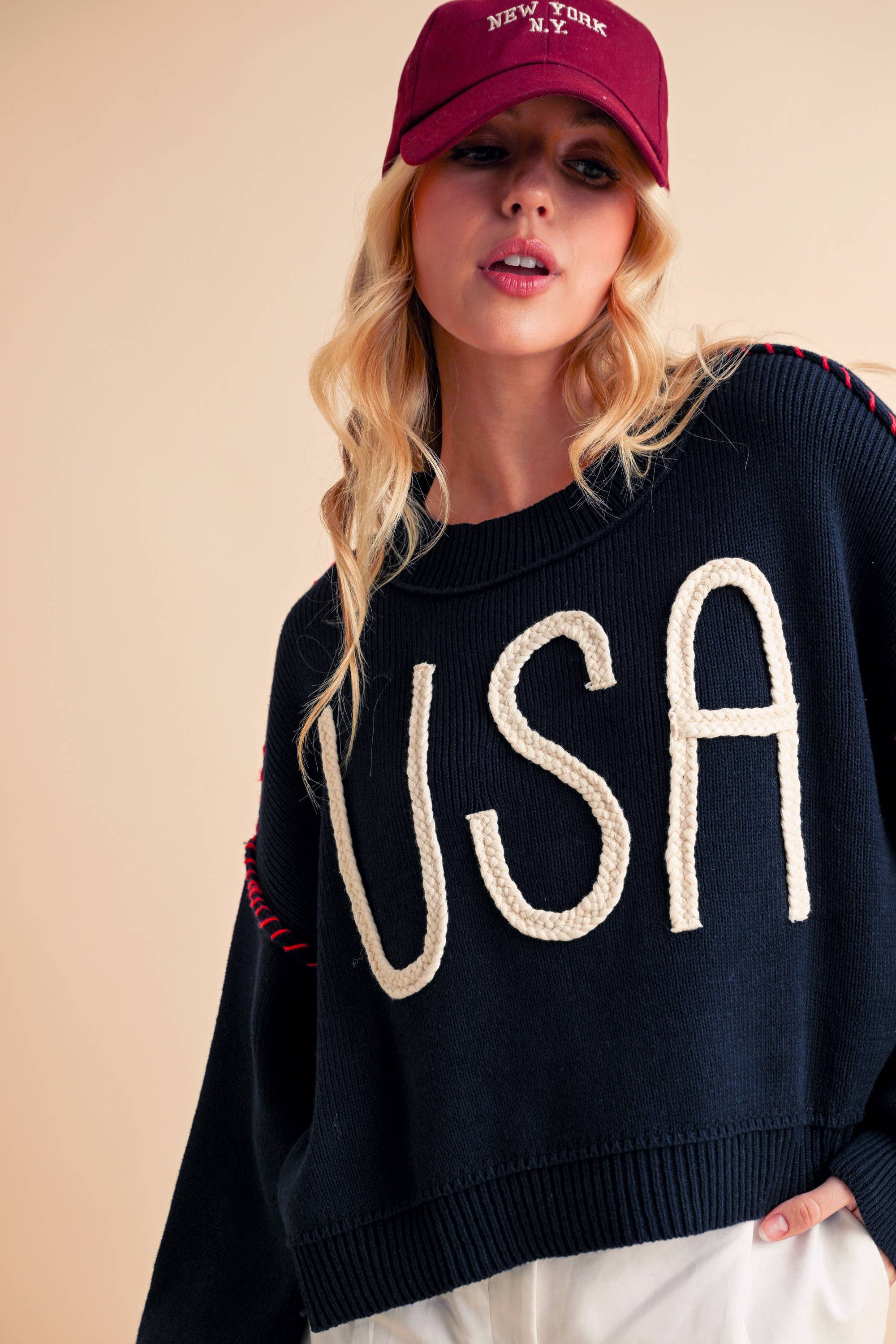 A woman wearing a navy sweater with the text 'USA' in white letters, paired with white shorts and a red cap.