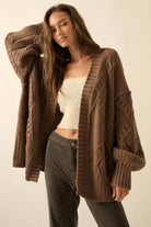 Woman wearing a brown cable knit cardigan over a white top and gray pants on a beige background