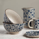 Ceramic bowls, pitcher, and mug with blue floral pattern on a neutral background