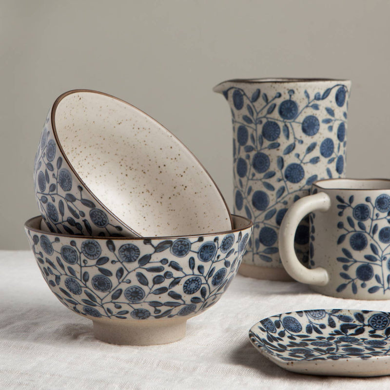 Ceramic bowls, pitcher, and mug with blue floral pattern on a neutral background