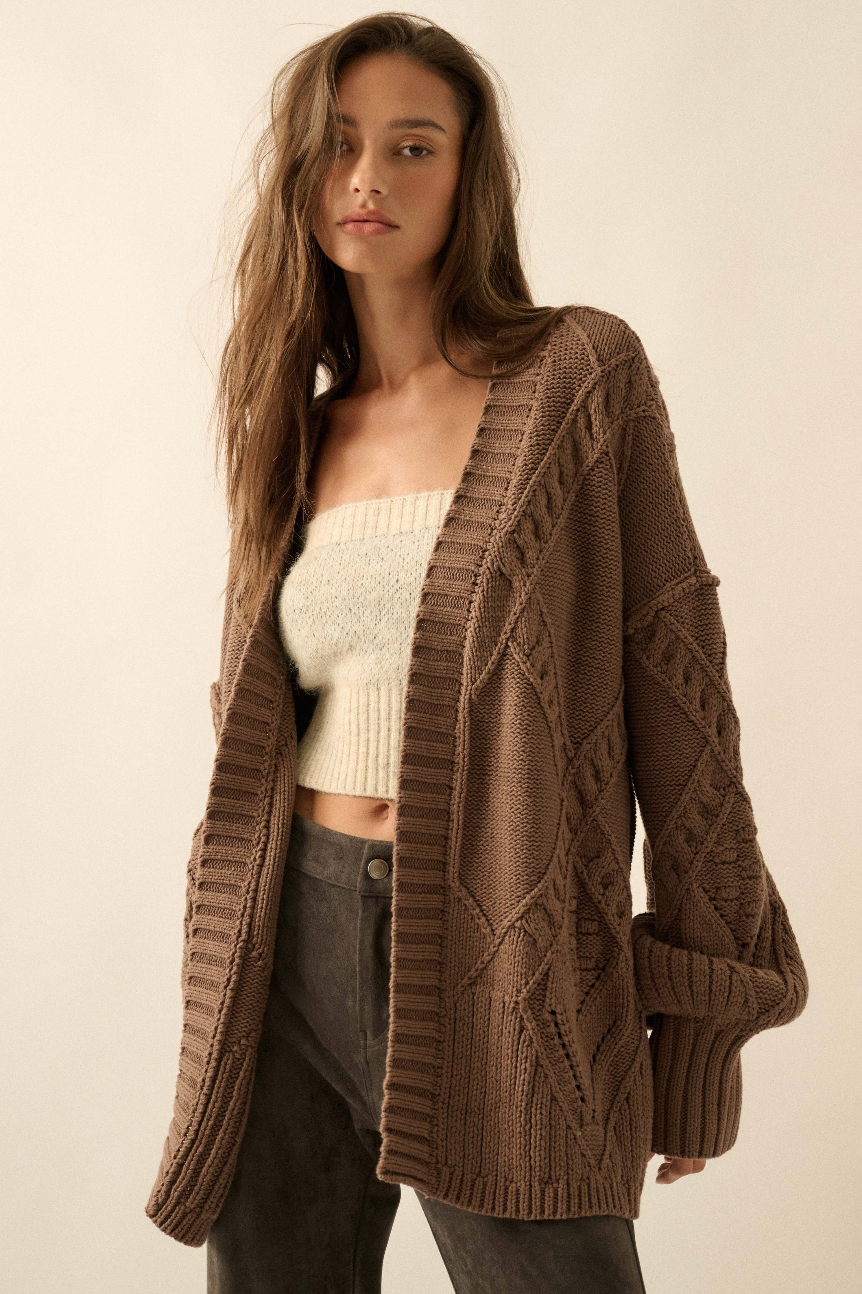 Woman wearing a brown knitted cardigan over a white top and gray pants on a beige background