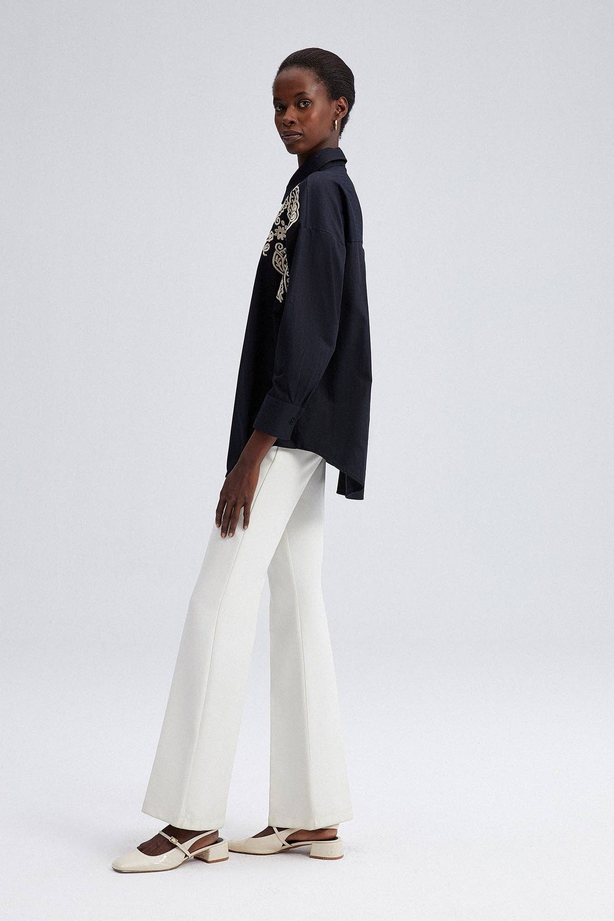 Model wearing black oversized shirt with cream embroidery on shoulders and front yoke.
