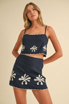 Woman wearing the Calista Set—navy two-piece with scalloped embroidered crop top and matching mini skirt.