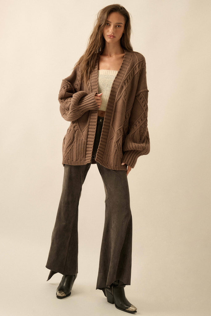 Woman wearing a brown knitted cardigan and flared pants on a beige background