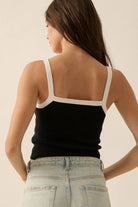 Black ribbed knit tank top with white trim on the straps and neckline, styled with light-wash denim jeans.