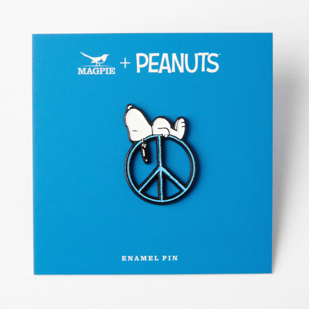 Snoopy enamel pin on a blue background labeled "Magpie + Peanuts," featuring a peace sign design.