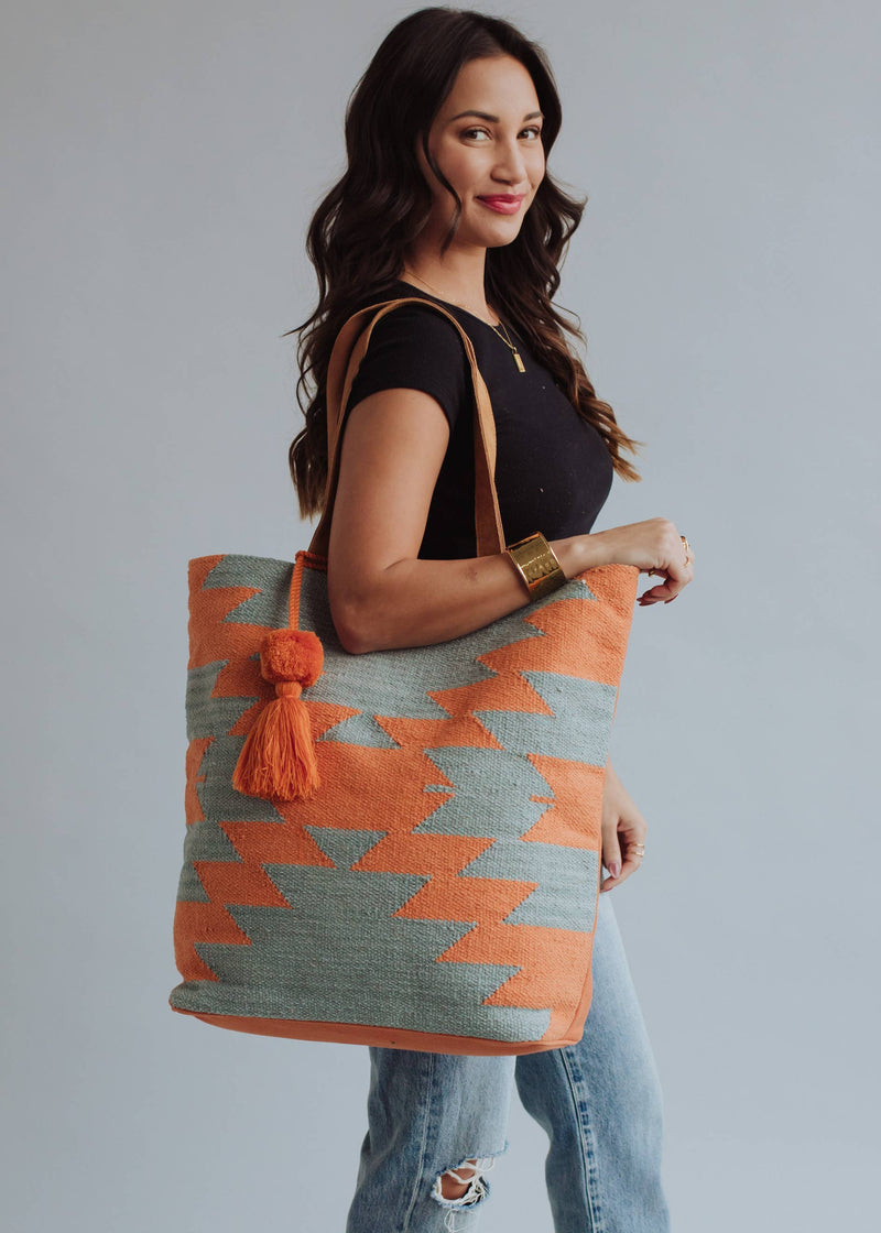 Tote bag with orange and sage green zigzag design and tassel, styled with denim jeans