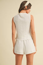 Model wearing a white sleeveless textured two-piece set featuring a cropped top and matching shorts with pockets.