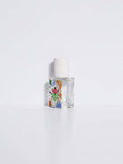 Maison Matine Nature Insolente perfume bottle with colorful leaf and beetle illustrations, placed on a vibrant yellow fabric and surrounded by green foliage.