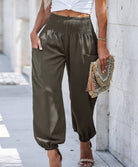 Woman wearing Serenity High-Waist Comfort Pants in beige and olive colors, paired with a white crop top and heels, carrying a decorative clutch.