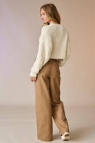 Woman wearing a cream popcorn knit cropped sweater with tan drawstring pants, hands in pockets.