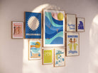 Helping Hands Print featuring diverse women standing together and holding a surfboard, framed in a wooden frame.