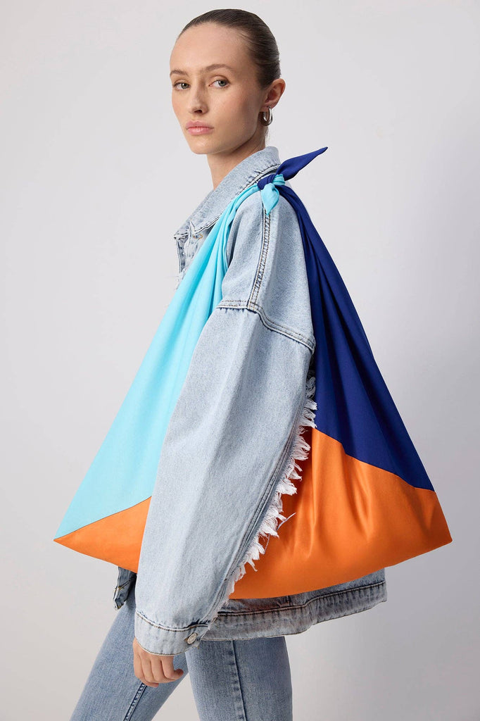 Colorblock tote bag in orange, light blue, and navy, worn over the shoulder with a knot strap.
