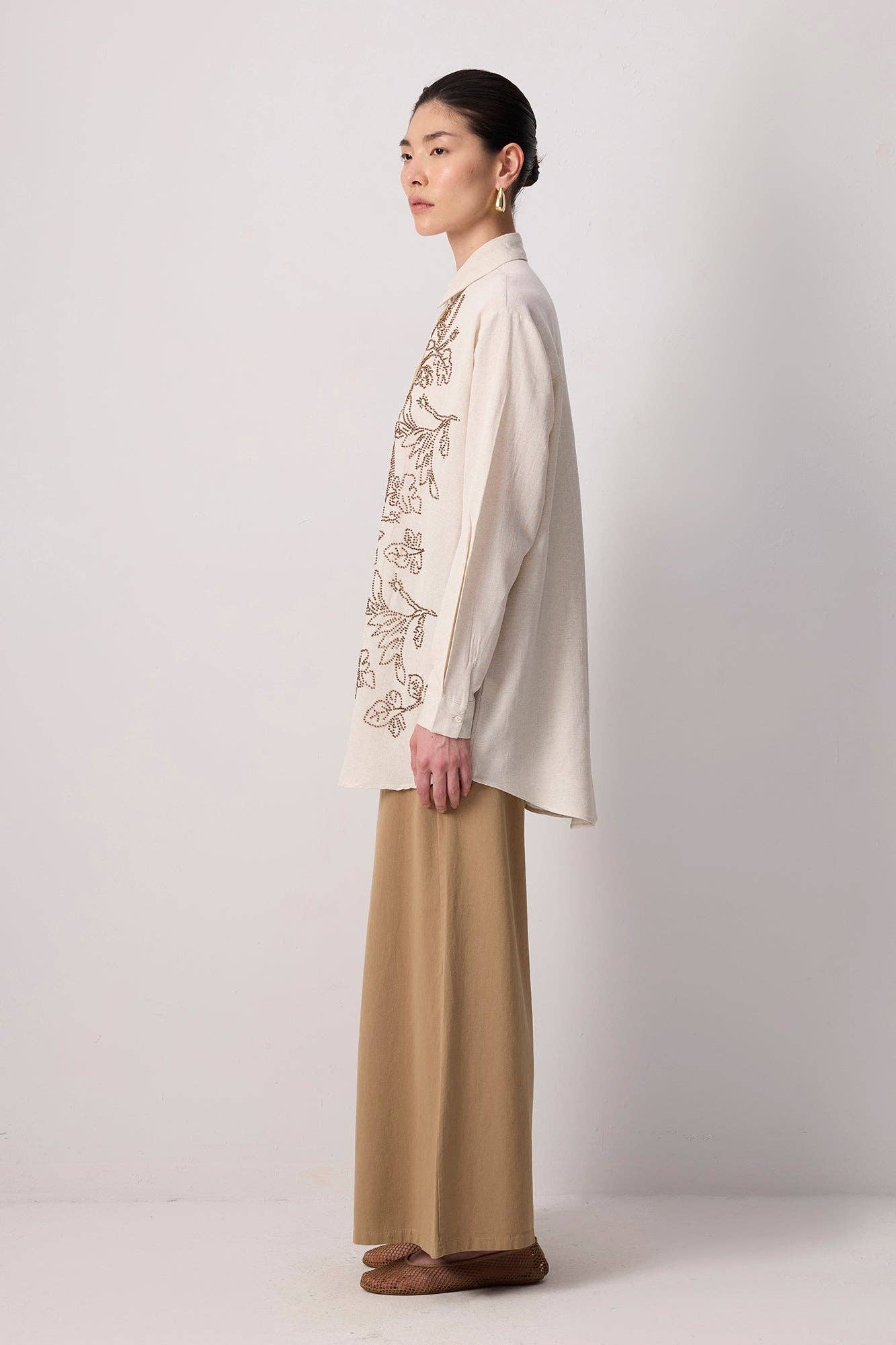 Model wearing a beige button-up shirt with floral embroidery and beaded detailing
