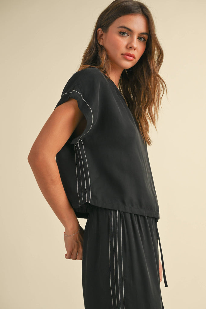 Model wearing a black two-piece lounge set with white contrast stitching, featuring a cap-sleeve top and drawstring wide-leg pants.