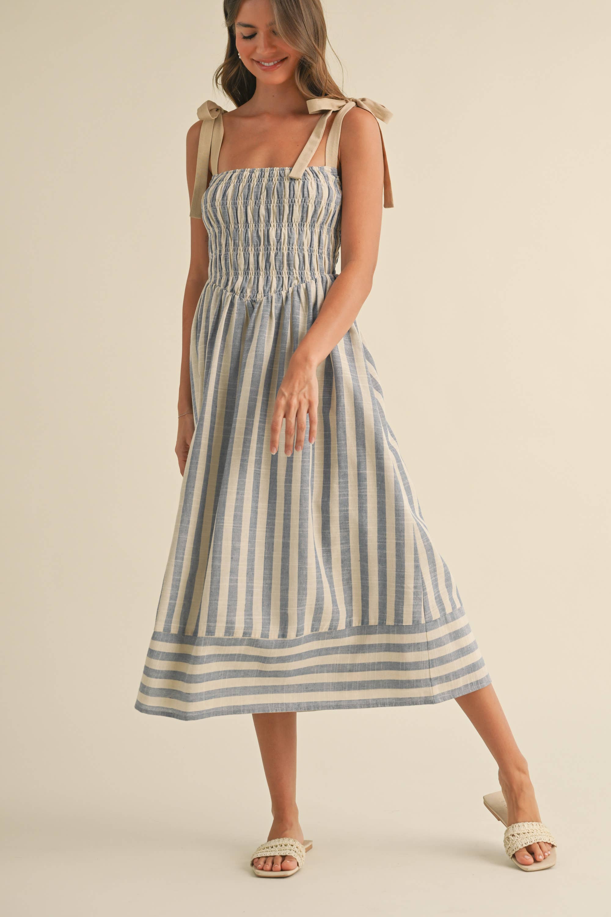 Woman wearing a blue and cream striped midi dress with smocked bodice and tie shoulder straps.