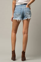Close-up of asymmetrical distressed denim shorts with frayed hem and high-waisted fit.