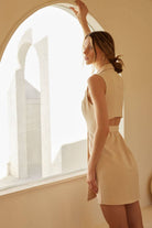 Woman wearing a beige sleeveless blazer-style mini dress with a waist tie and lapel collar.