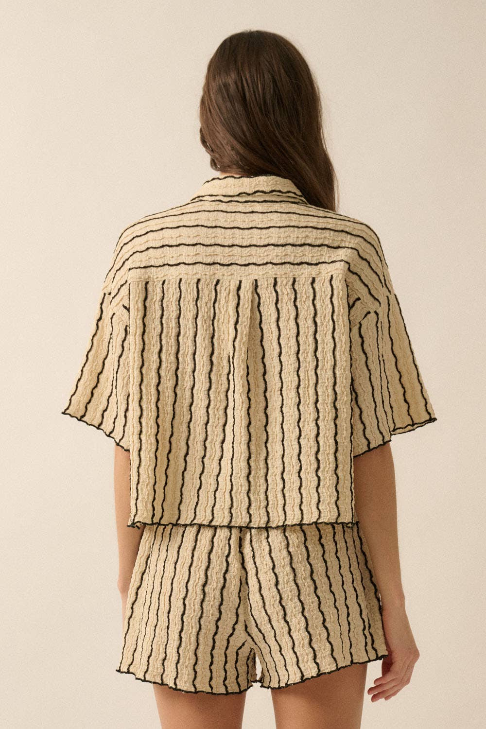Woman wearing a beige striped two-piece lounge set with button-up shirt and matching drawstring shorts.